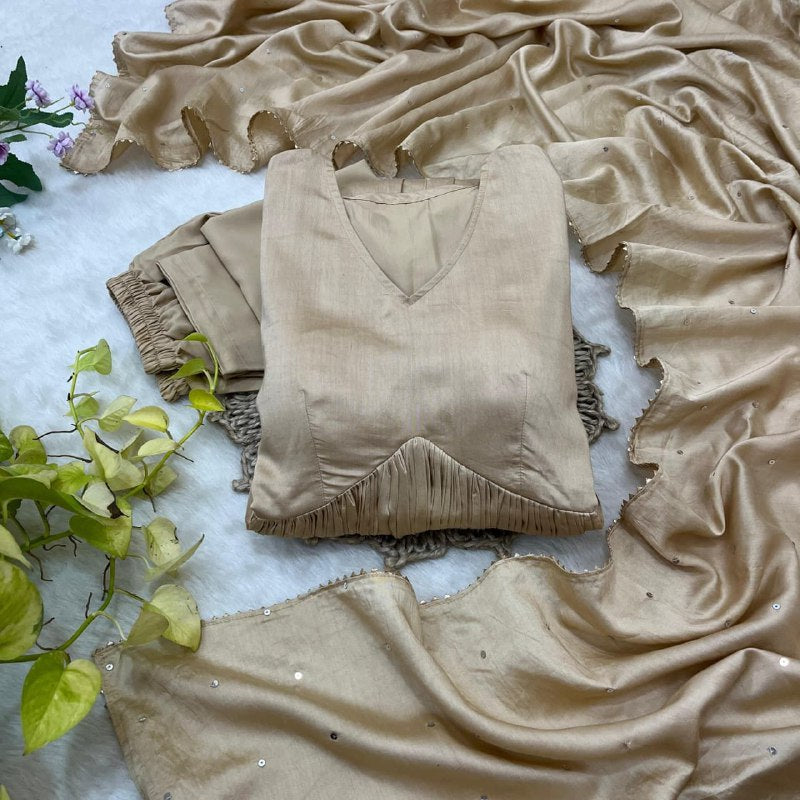 Beige fringe top and pants on a textured surface with green leaves.Beige Anarkali Suit Set Roohri 
