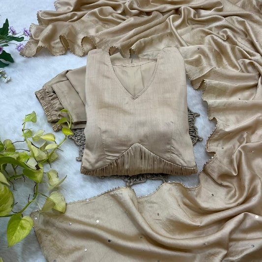 Beige fringe top and pants on a textured surface with green leaves.Beige Anarkali Suit Set Roohri 