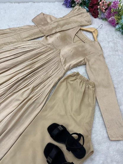 Beige pleated dress, pants, and black sandals on a textured surface with flowers in the background. Beige Anarkali Suit Set Roohri 