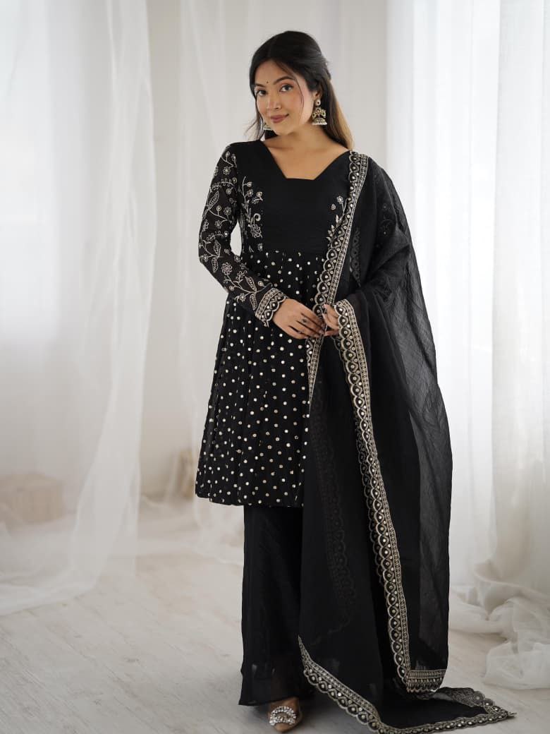 Woman wearing a black traditional outfit with embroidery against a white curtain background Black Sharara Suit Set Roorhi