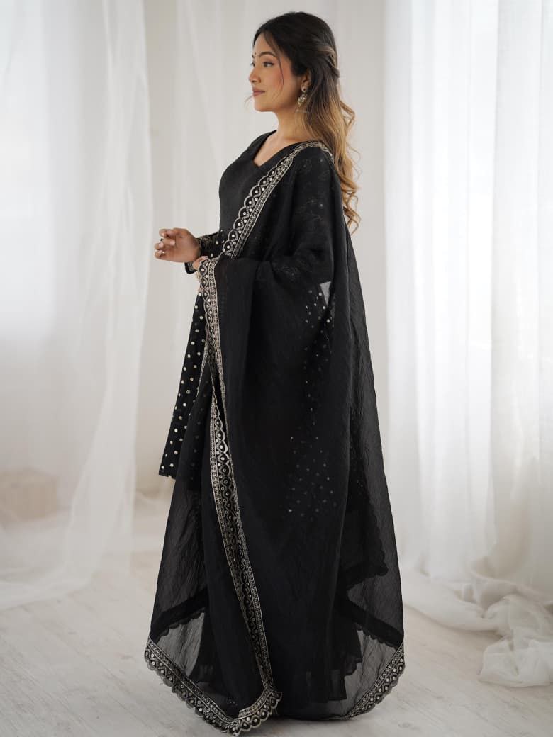Woman wearing a black embroidered outfit with sheer sleeves against a white curtain background Black Sharara Suit Set Roorhi