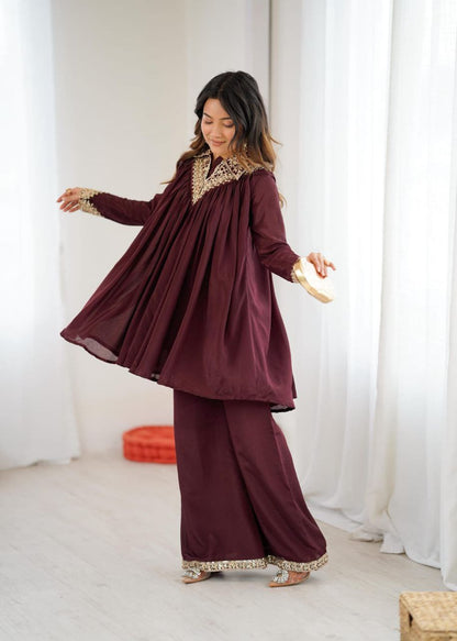 Woman wearing a burgundy traditional outfit with gold embroidery in a white room. Co-ord Set Roohri