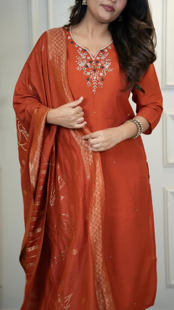 Woman wearing a red traditional outfit with embroidery, standing against a white background. Orange hand embroidered suit set Roohri