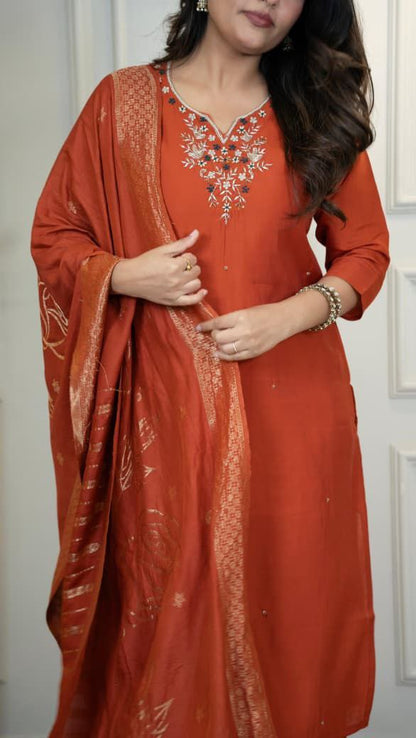 Woman wearing a red traditional outfit with embroidery, standing against a white background. Orange hand embroidered suit set Roohri