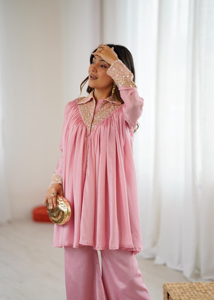 Woman wearing a pink outfit with gold accents in a room with white 
curtains. Pink Co-ord Set