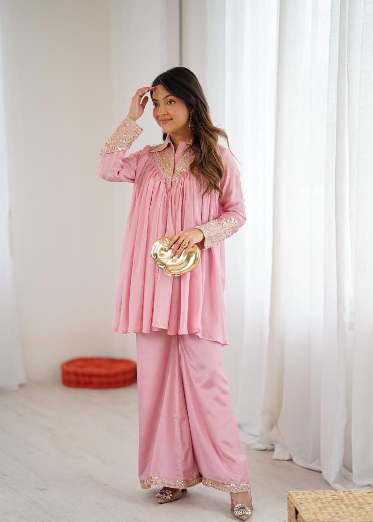 Woman in a pink traditional outfit with gold accents, holding a gold clutch against a white curtain background. Pink Co-ord Set

