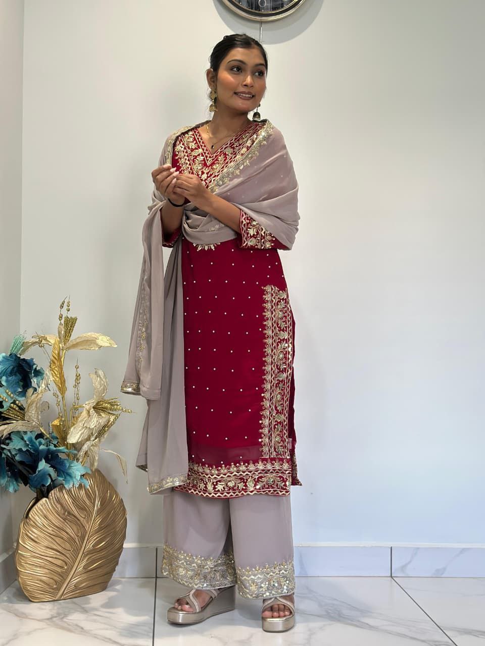 Woman in traditional outfit with red and white dress and beige dupatta, standing indoors. Red Palazzo Suit Set Roohri
