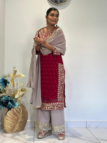 Woman in traditional outfit with red and white dress and beige dupatta, standing indoors. Red Palazzo Suit Set Roohri