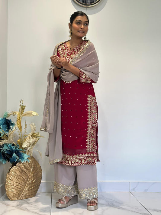 Woman in traditional outfit with red and white dress and beige dupatta, standing indoors. Red Palazzo Suit Set Roohri